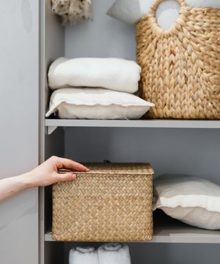 A gray shelf with white bedding and wicker baskets