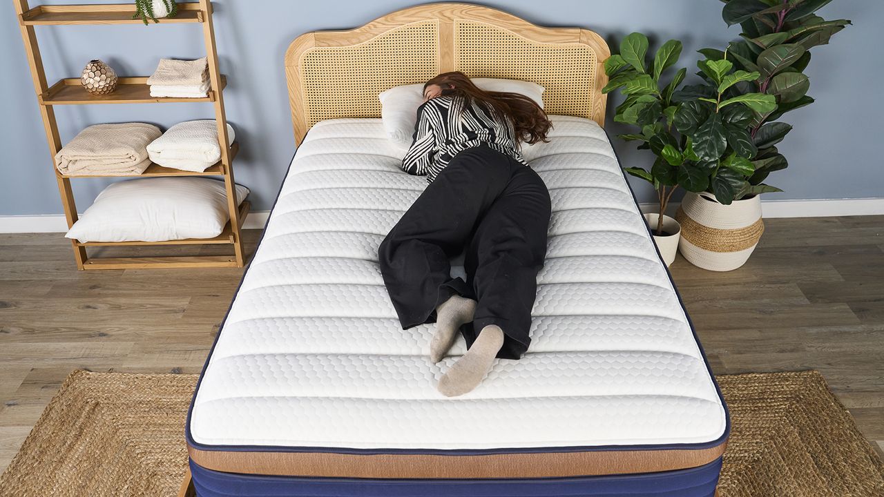 A girl wearing black and white pyjamas laying on her stomach on Brooklyn Bedding CopperFlex Pro Hybrid mattress with white surface and rattan bedframe