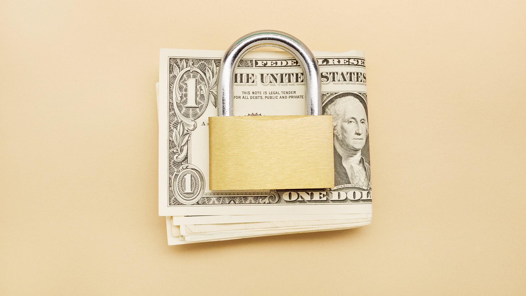 A padlock sits on top of a folded stack of cash.