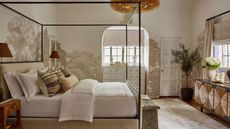 Neutral bedroom with four poster black metal bed, botanical neutral wallpaper, cream carpet, textured sideboard
