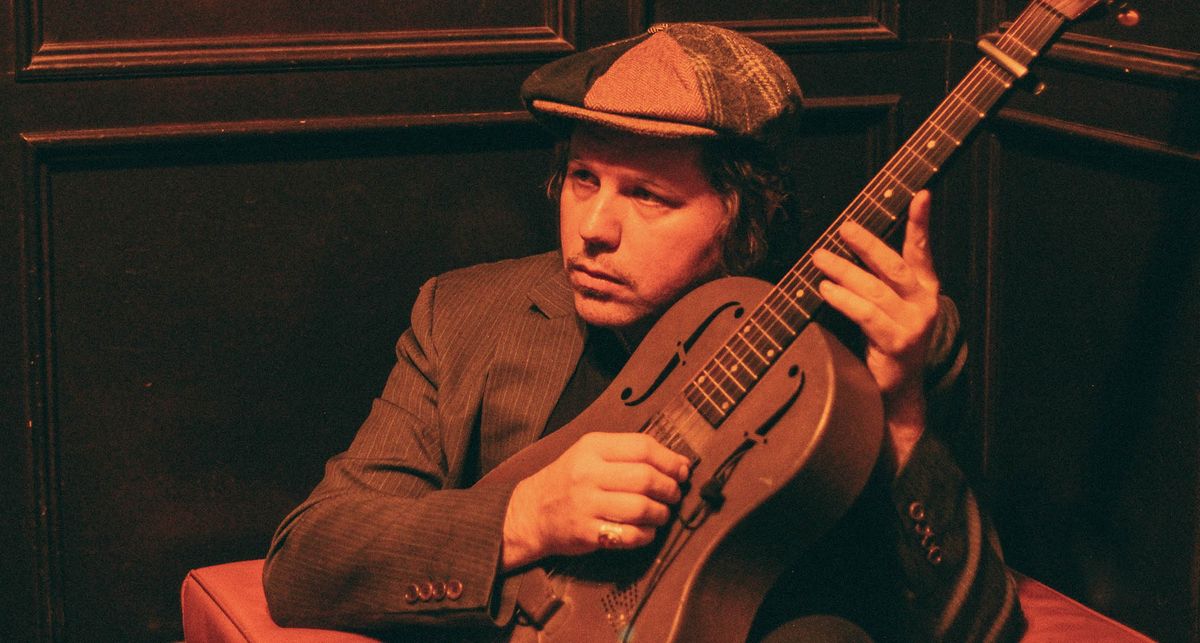 Jim Oblon plays a resonator guitar in a dimly lit image