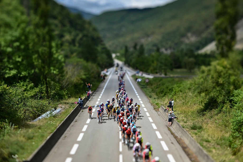 This photograph taken with a tilt-shift lens shows the pack of riders (peloton) cycling during the 18th stage of the 112th edition of the Tour de France cycling race, 171.5 km between Vif and Courchevel Col de la Loze, in the Alps, southeastern France, on July 24, 2025. (Photo by Marco BERTORELLO / AFP)