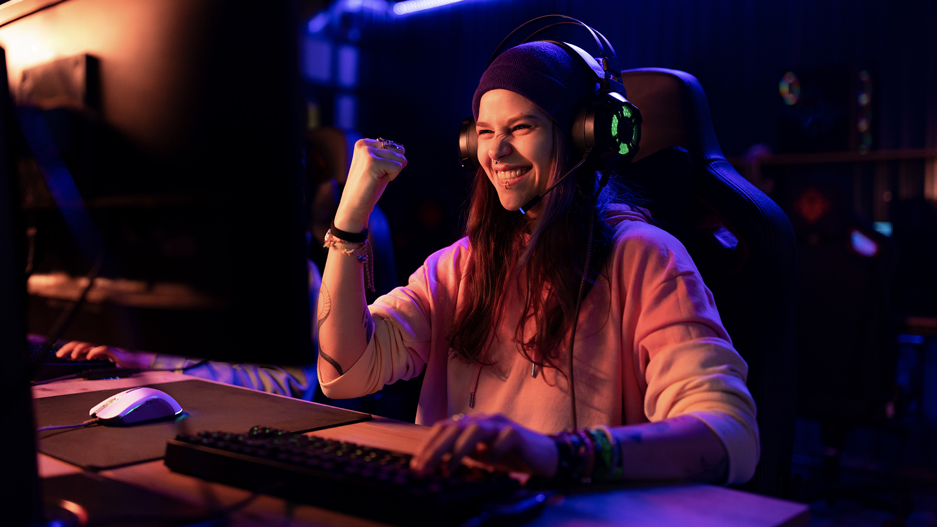 Happy female gamer celebrating her success in video game over PC at entertainment club.