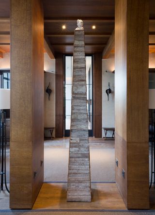 A sculpture on top of a triangular wooden structure between two wooden panels with a doorway behind it.