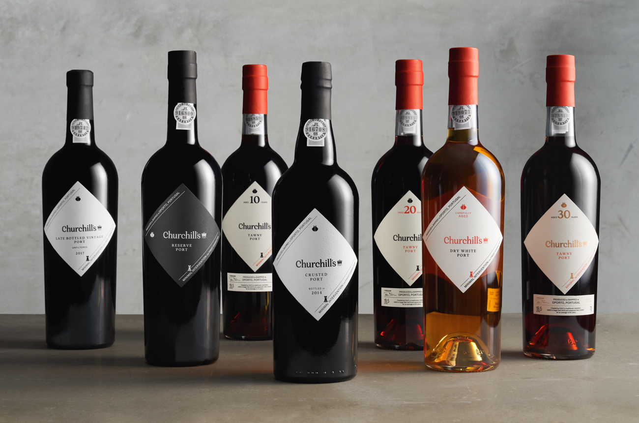 Seven bottles of Port lined up against a grey background