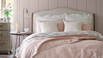 Pink panelled bedroom wall with bed with light pink bedding, bedside table, dresser