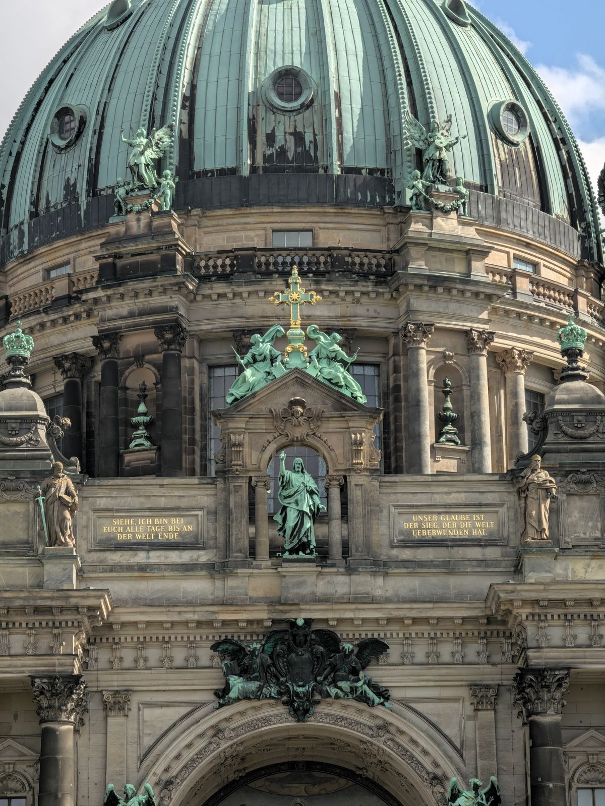 Close-up architectural detail of Berlin Cathedral showing its green copper dome, statues, columns and decorative stonework.