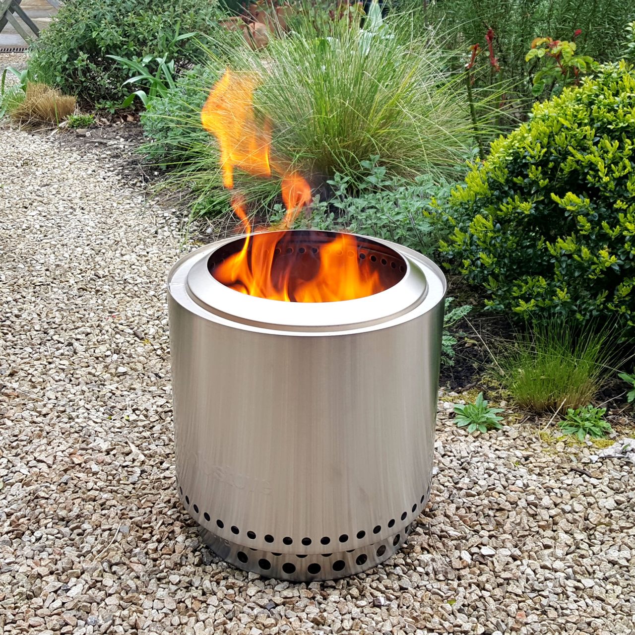 The stainless steel Solo Stove Ranger fire pit with flames coming out of the top in a gravel garden