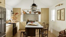 A neutral kitchen design with beige cabinetry and black and copper accents. A black kitchen island and copper kitchenware hanging over the stove