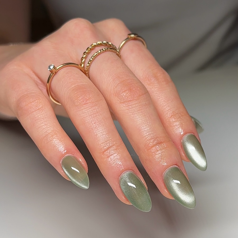 a hand with four gold rings featuring a reflective green sea glass-inspired manicure