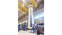 a white rocket booster is suspended a few feet from the ground inside a huge hangar