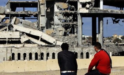 Palestinians sit next to the remains of a service building struck by Israeli war planes in March: Israel and Hamas reportedly called a ceasefire Monday.