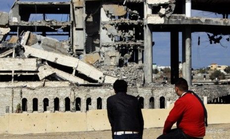 Palestinians sit next to the remains of a service building struck by Israeli war planes in March: Israel and Hamas reportedly called a ceasefire Monday.