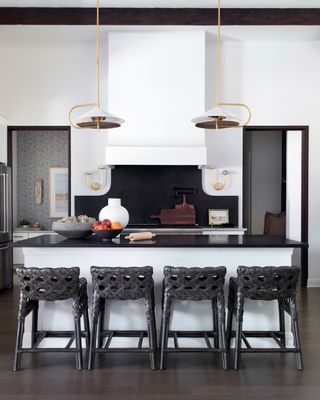 white kitchen with black door frames left and right of stove, white island with black top and black woven stools