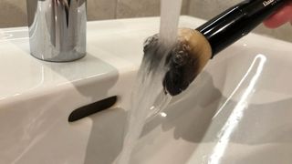 A makeup brush being rinsed under water