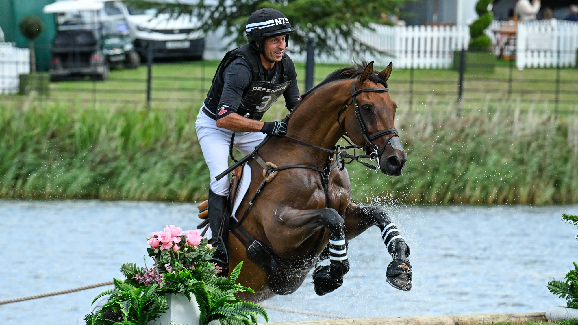 Tim Price, a rider in a black top, rides bay horse Global Quest up a step fence on the Burghley cross-country course