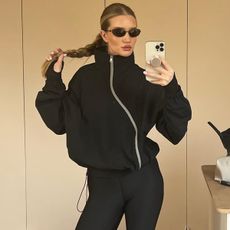 Model Rosie Huntington-Whiteley wears black anorak and black leggings while taking mirror selfie.