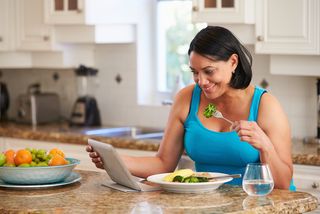 A woman checks her tablet while eating a healthy meal.