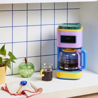 a colorful, retro-inspired coffee maker in a kitchen with white tiles and blue grout lines