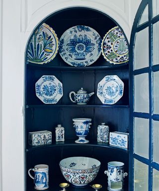 a built in storage dresser with glass fronted door painted in a deep blue with blue and white accessories
