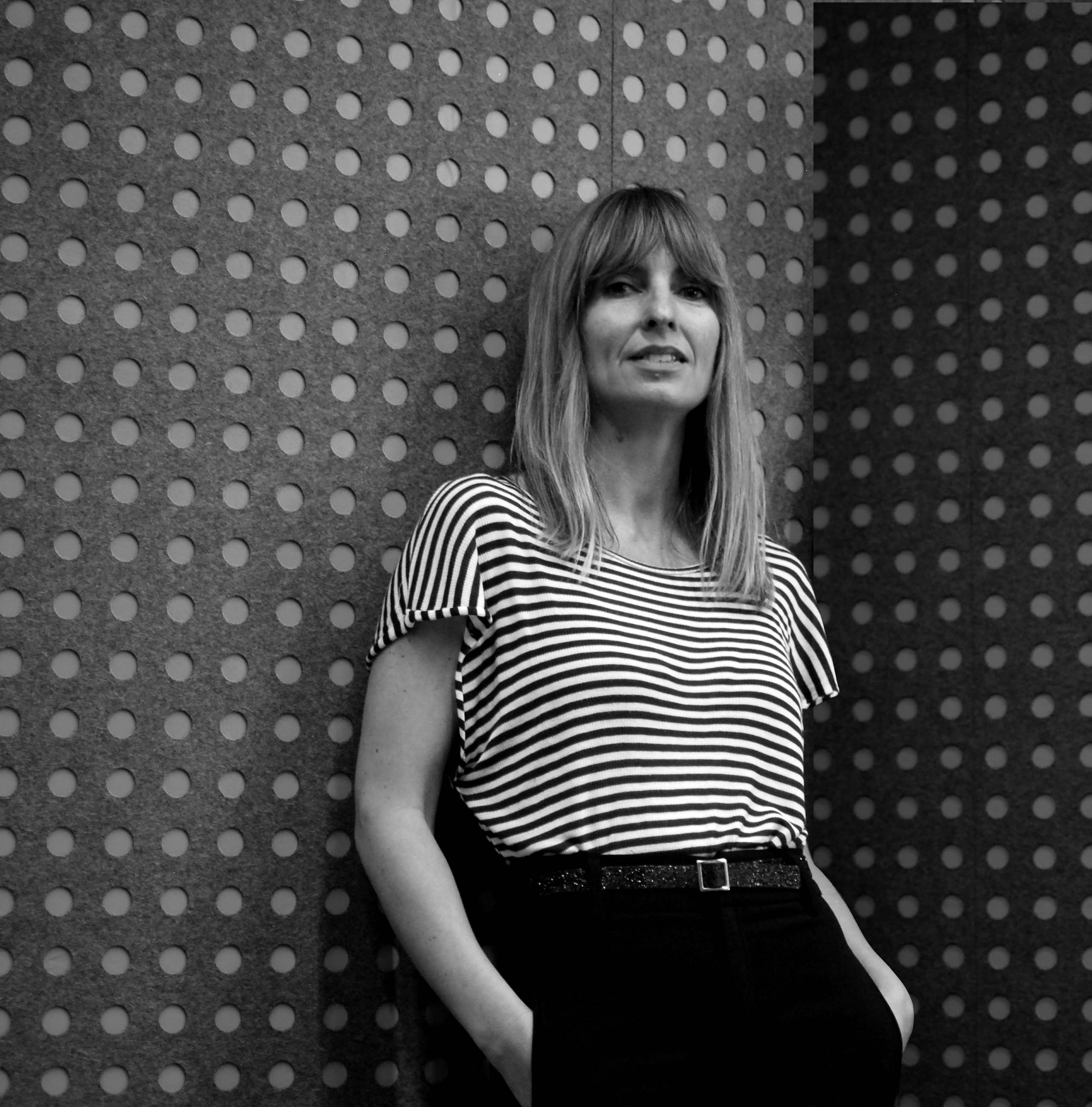 Marga Castaño stands against a wall, in a black and white photo.