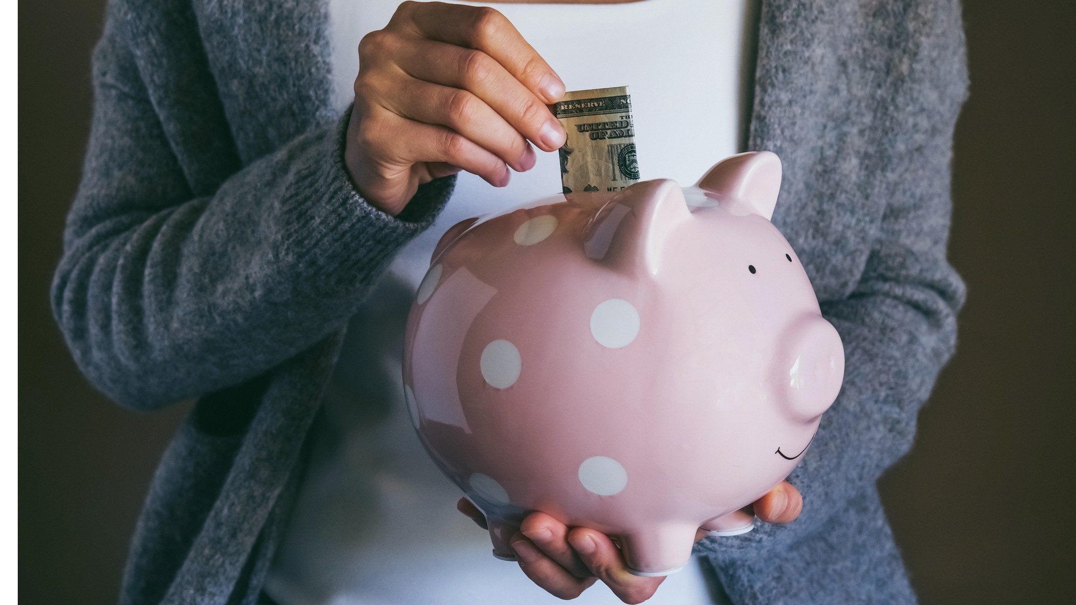 a woman placing dollar bills into a piggy bank