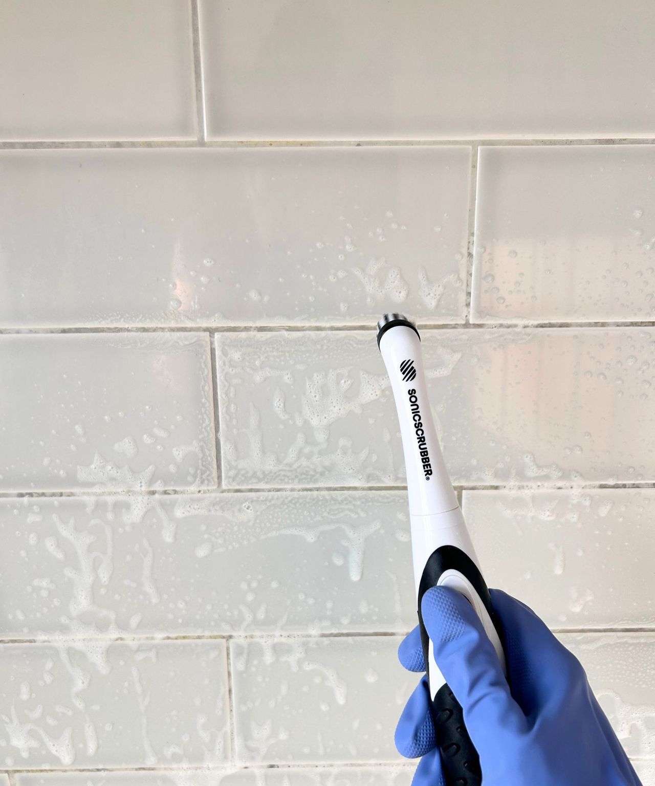 Person with purple glove on using a SonicScrubber to get in between tiles