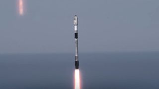 A used black and white SpaceX rocket launches with the ocean horizon in the background.