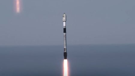 A used black and white SpaceX rocket launches with the ocean horizon in the background.