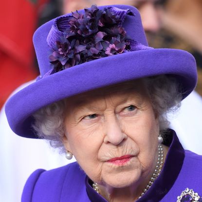 Queen Elizabeth in a purple hat and coat, pursing her lips