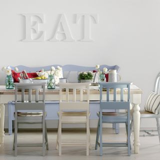 White dining room with wall lattering, wooden chairs and table and blue bench
