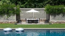 A garden with a large swimming pool and a outdoor dining area and garden fence painted in gray