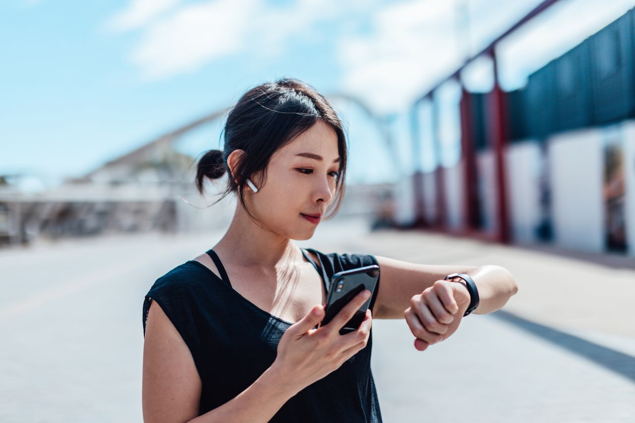 Woman checking fitness apps &amp; tracker on her wrist with street behind her