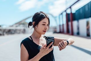 Woman checking fitness tracker on her wrist with street behind her