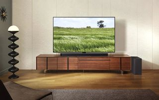 Samsung Q800C soundbar on a wooden TV console, in front of a TV