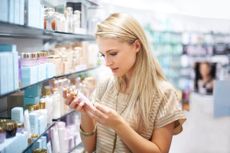 A woman reads the label on a bottle of skin care product. 