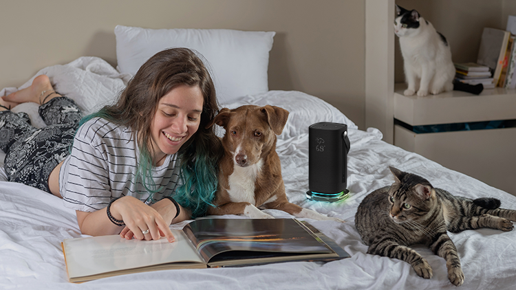 Une jeune femme lisant sur un lit avec un chien et deux chats à côté de l'enceinte Acer Halo Swing Speaker.