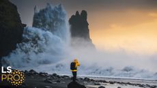 A massive wave hits a cliff on the coast of Iceland at sunset.