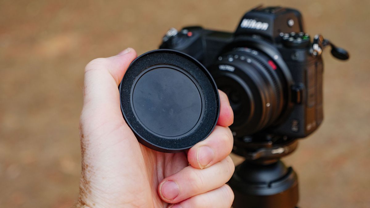 Viltrox AF 26mm F2.8 EVO 'pancake' lens attached to a Nikon mirrorless camera, with the magnetic lens cap being held in front of it
