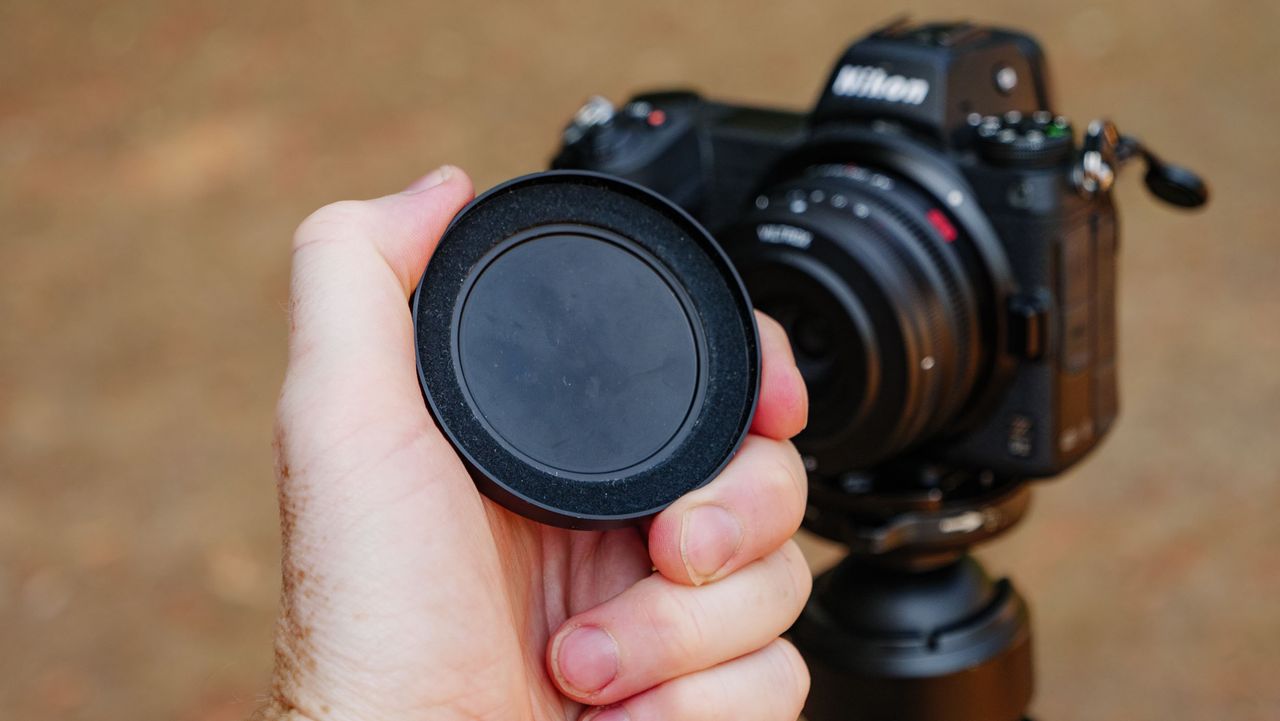 Viltrox AF 26mm F2.8 EVO 'pancake' lens attached to a Nikon mirrorless camera, with the magnetic lens cap being held in front of it