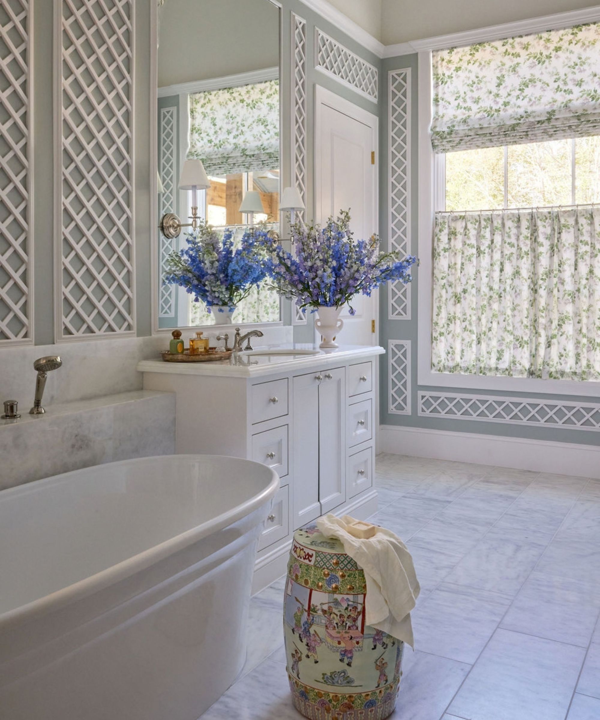 Elegant bathroom featuring a freestanding white soaking tub, white vanity with blue flowers, lattice wall molding, and floral window shades