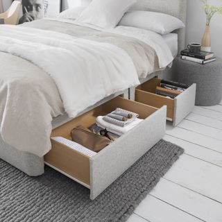 small bedroom with under bed storage showing, neutral scheme, white painted floorboards, grey rug, pale grey bed, mid grey footstool/nightstand