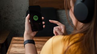 A woman wearing headphones opening the Spotify mobile app 