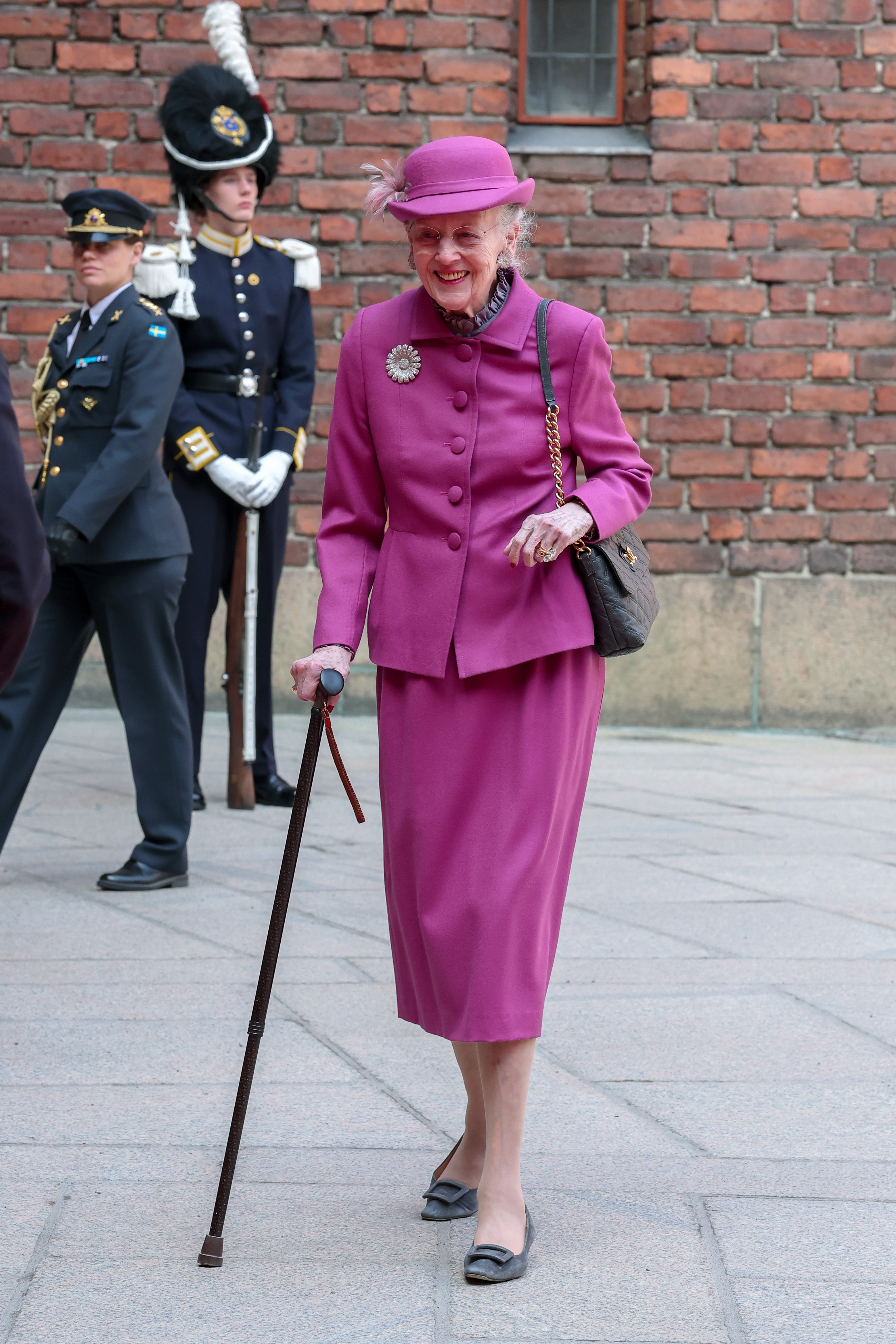 Queen Margrethe wearing a pink skirt suit walking with a cane