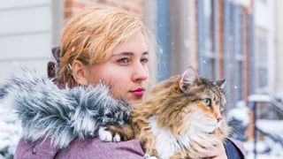 a woman holds a large cat outside in the snow