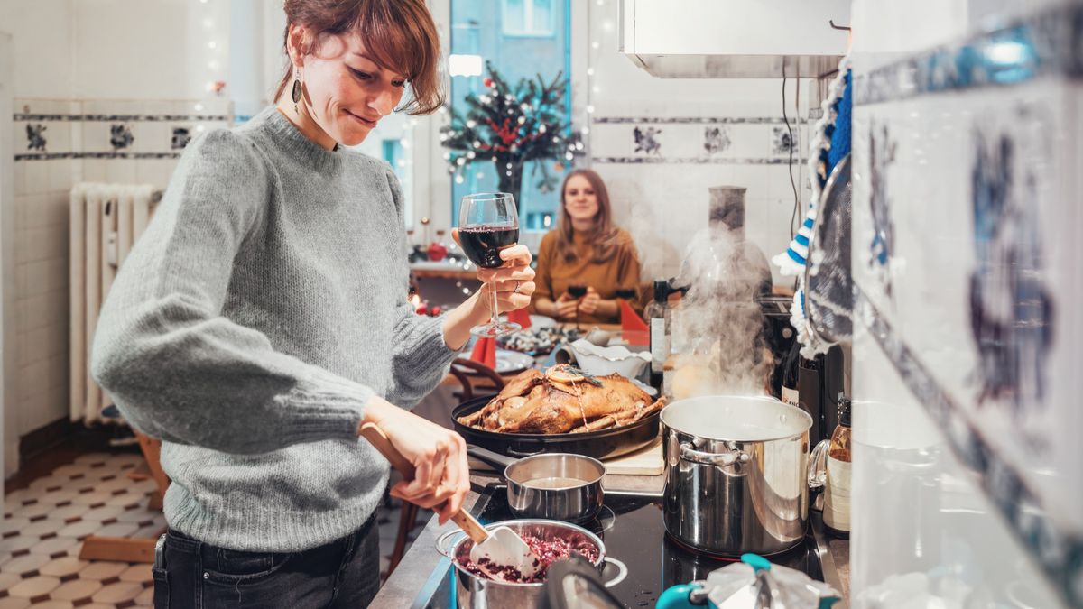 Happy woman preparing Christmas dinner while drinking glass of wine