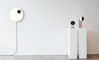 Circular lights. One piece is set on the wall to the left, while the other two are set on gray stands to the right.