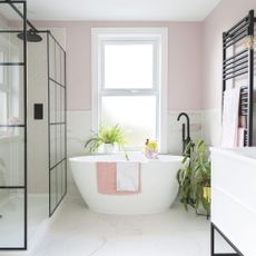 Houseplants in a white and pink bathroom including calathea plant next to large contemporary freestanding bath