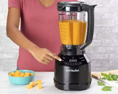 A Nutribullet Smart Touch Blender in a kitchen. A woman is using it to blend squash for soup