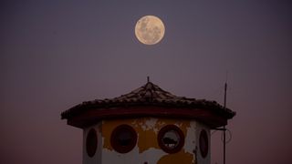 a full moon rises above a small pagoda